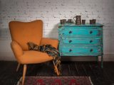 Composition of vintage orange armchair, blue cabinet and ornate scarf in studio